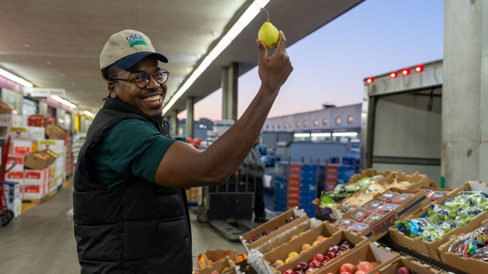 An African-American man with an USDA hat smiling and holding a fruit
