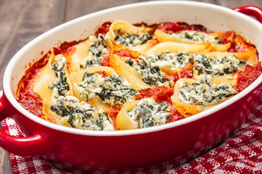 Pasta shells in red sauce, stuffed with spinach and cheese in a red baking dish, resting on a red and white kitchen towel.
