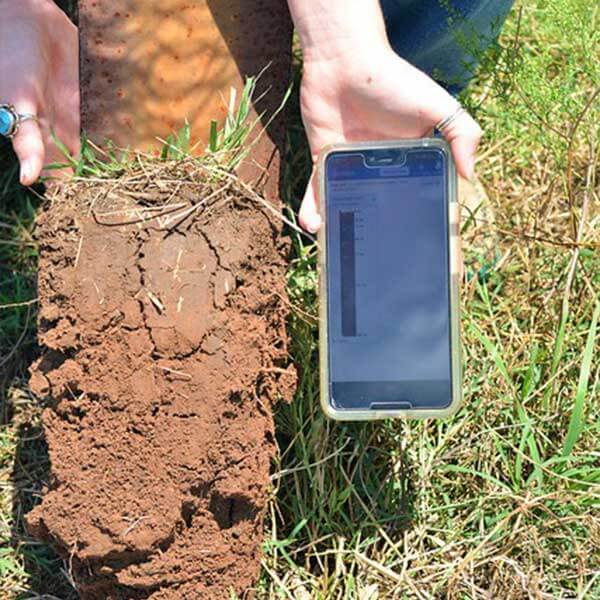 Person holding soil in one hand and a cell phone with the Soil app in the other hand