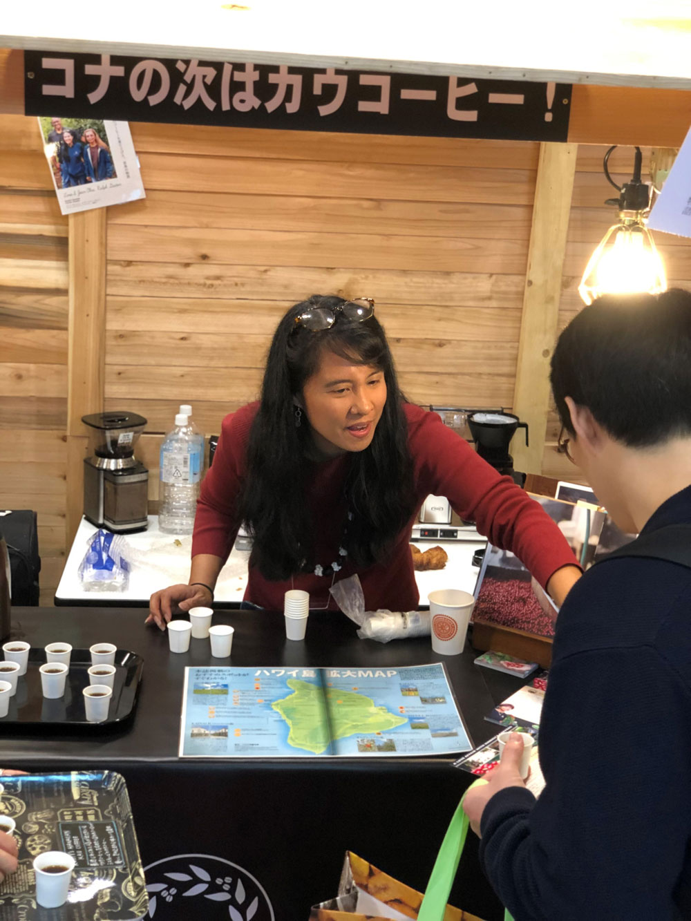 A woman stands at a table with coffee samples and a map of Hawaii