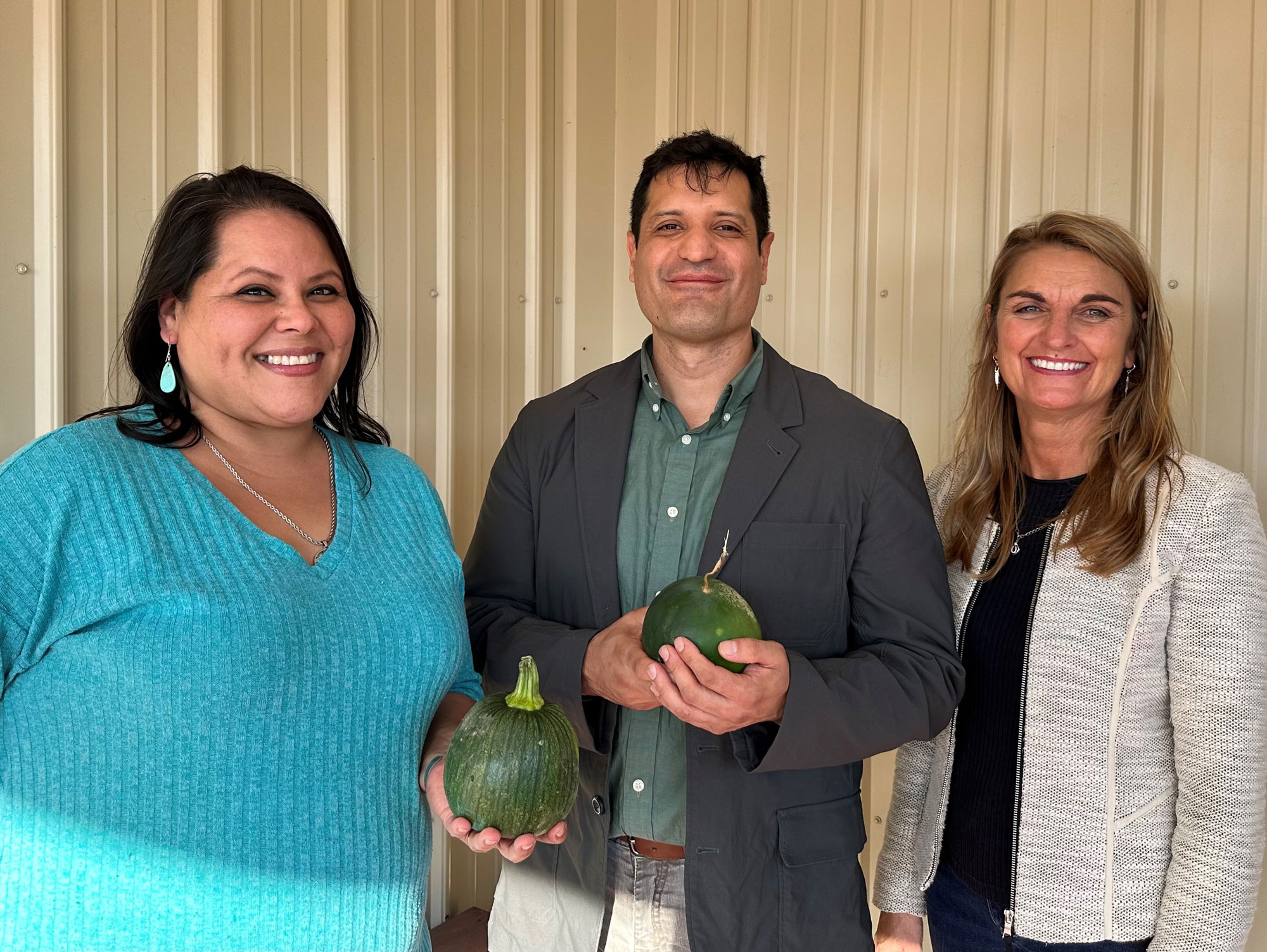 Jessika Free-Bass and Mario Ramos hold garden produce and stand with Cheryl Kennedy