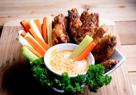 Bowl of chicken wings, cup of hot sauce, carrot and celery sticks with parsley