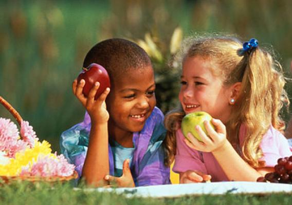 A boy and girl smiling and holding fruits in their hands