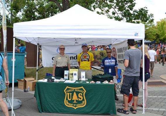 Kristy Wumkes (left), partnership coordinator on the Canyon Lands Ranger District, and volunteers greets visitors to the U.S. Forest Service booth at the Fort Collins stage finish line. (U.S. Forest Service/Reghan Cloudman)