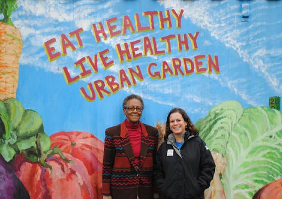 Livia Marqués and Juanita Ewell stand in front of the tool shed at Eat Healthy Live Healthy Urban Garden in the 900 block of Cherry Hill Road, Baltimore City, Maryland. The mural was painted by Towson University student John Rice. 