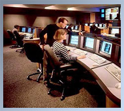 photo of man standing next to a seated woman pointing to one of multiple computer monitors