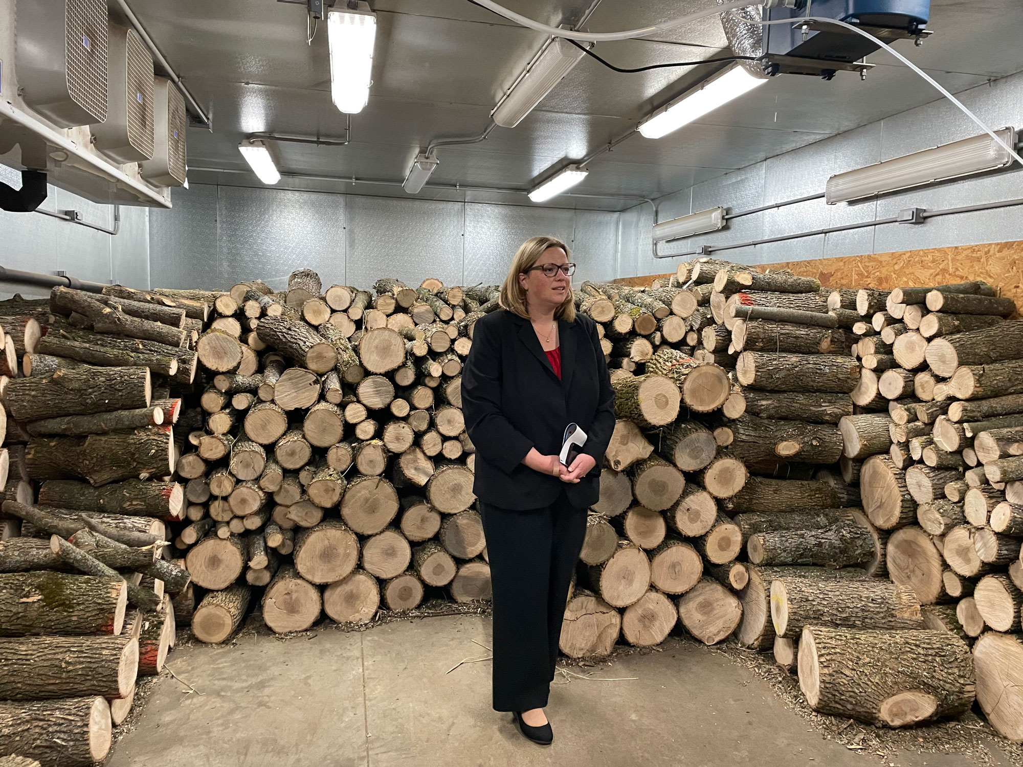 Under Secretary Jenny Moffitt standing in front of donated ash tree logs from Wisconsin