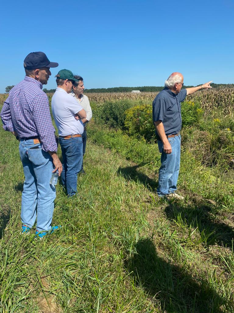 Farmer Bobby Hutchison standing in a wheat field, surveying his climate-smart, conservation-focused crops and discusses his farming success with members of a delegation from Argentina, Paraguay, and Uruguay