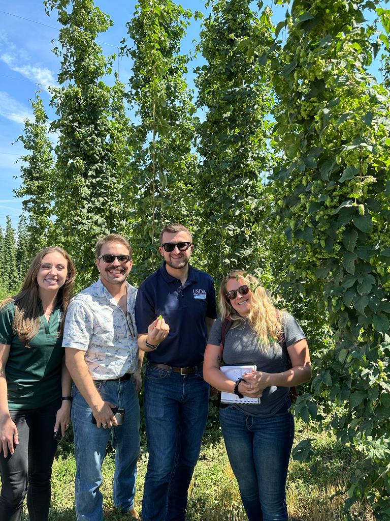 Foreign Agricultural Service’s Junior Professional Advancement Community team pose in front of hops vines at Loftus Ranches in Yakima Valley, Washington