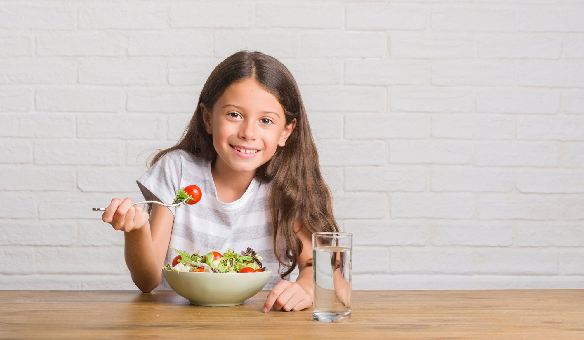 A girl eating a salad with a glass of water