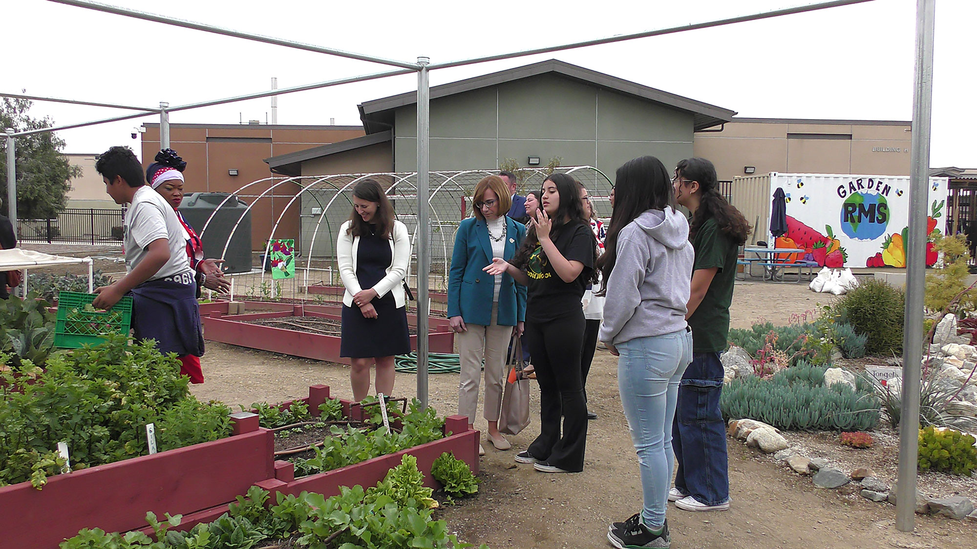 FNS Administrator Cindy Long and several Rialto Middle School students stand in front of planter boxes outside in a school garden