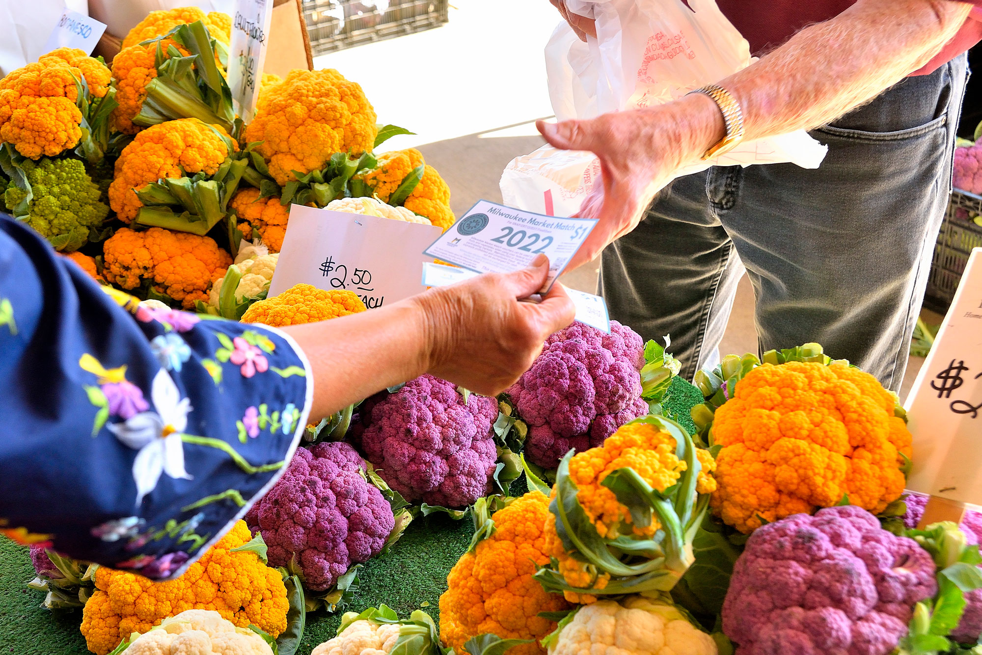 Person handing voucher to farmers market vendor to purchase cauliflower