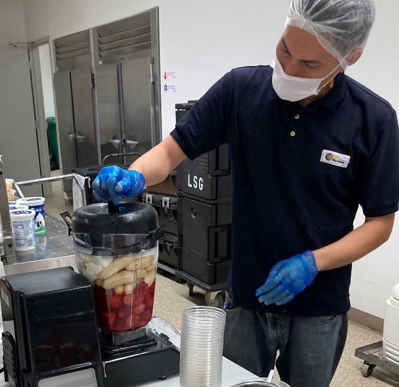 A kitchen staff member loading a blender with fresh fruit as he prepares smoothies for breakfast at a CNMI school
