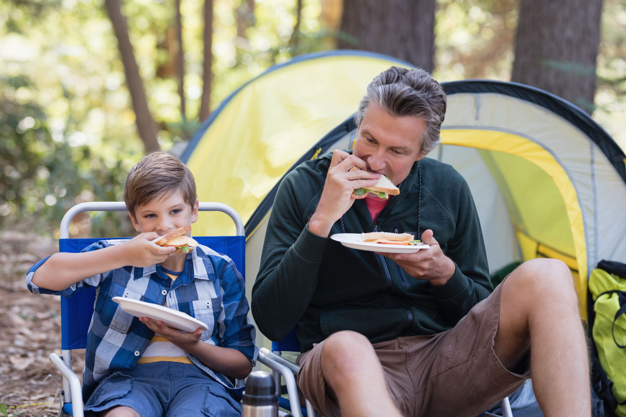 A father and son eating lunch while camping in a forest
