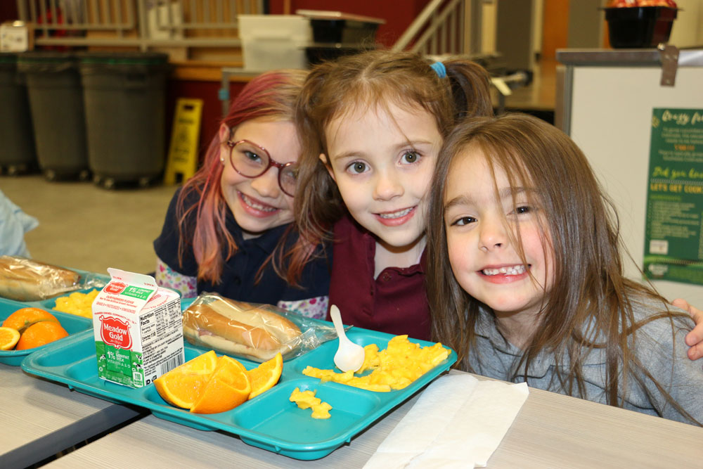Three girls enjoy school lunch at table