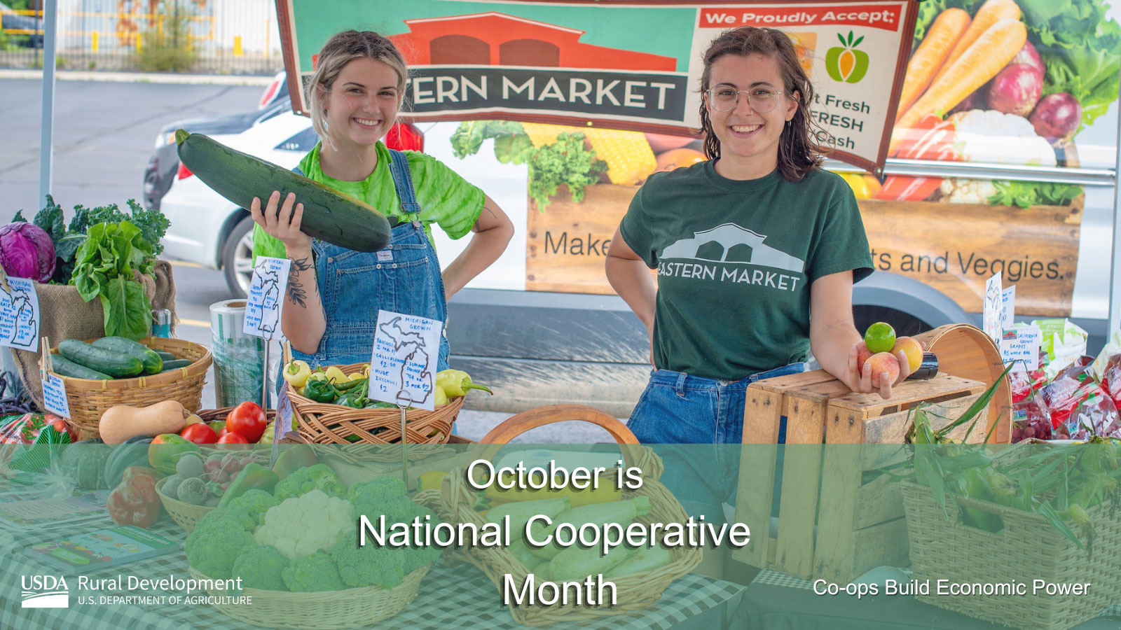 A woman smiling holding a cucumber and another woman smiling at the market with October is National Cooperative Month text overlay