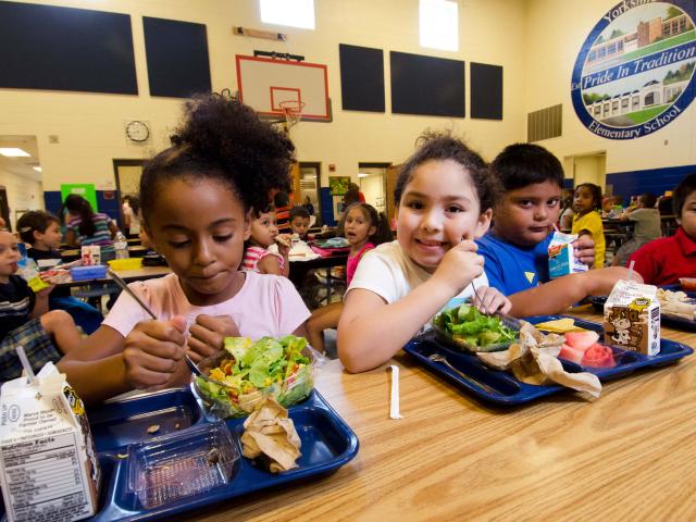 Four elementary school students eat lunch in a school cafeteria
