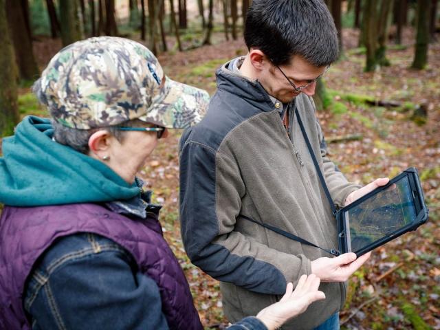 Two people looking at a laptop in a forest
