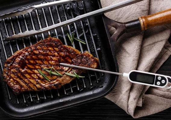 A steak on the grill with a food safety thermometer
