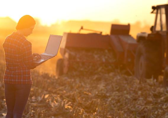 A farmer using a laptop in front of farm equipment