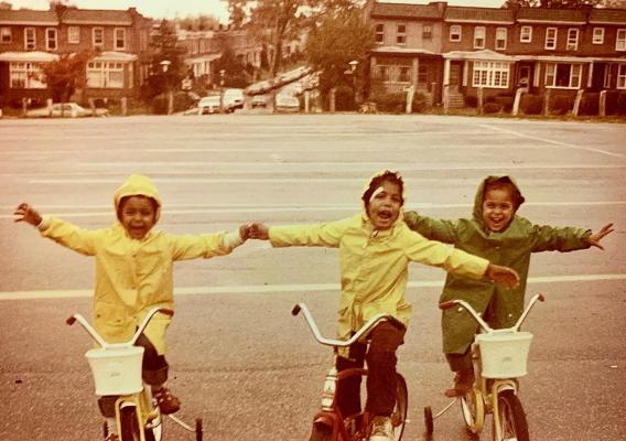 Three young children riding bikes in raincoats