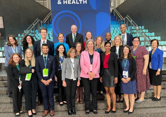 A group of 21 USDA Food and Nutrition Service employees dressed in professional attire and wearing conference badges pose together on a marble staircase in front of a blue conference banner at the White House Conference on Hunger, Nutrition, and Health