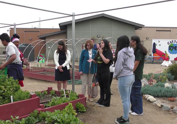 FNS Administrator Cindy Long and several Rialto Middle School students stand in front of planter boxes outside in a school garden
