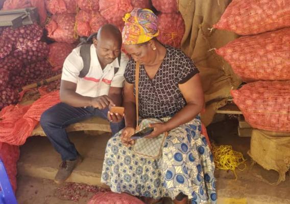 Agromovil Tanzania Country Lead, Wilbert Mdete, teaches a woman farmer how to use the app so that she can find buyers for her onions