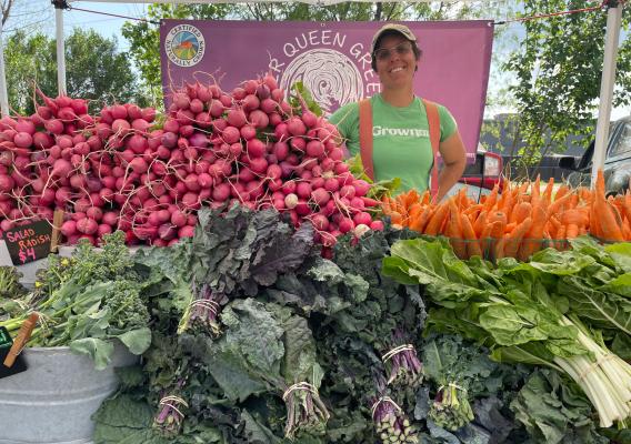 Co-owner Cheryl Nunes standing behind produce at the River Queen Greens farmers market stand