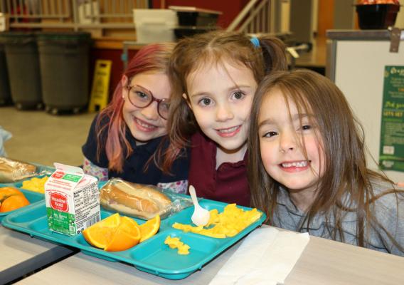 Three girls enjoy school lunch at table