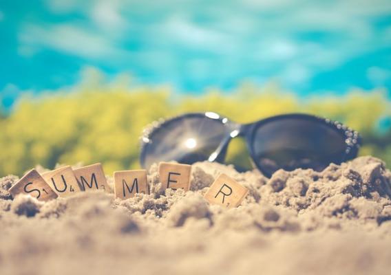 Sunglasses and the word summer spelled out in tiles on sand