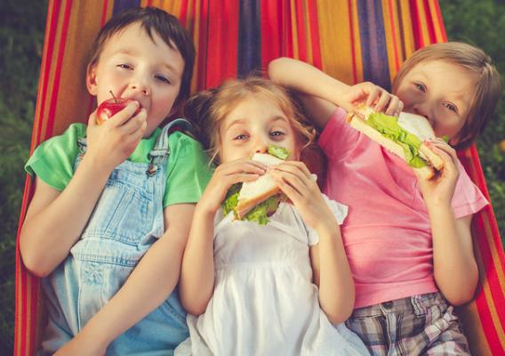 Three happy children eating apple and sandwiches in hammock