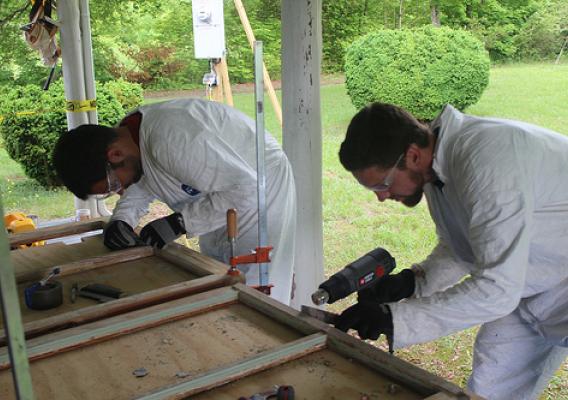 Military veteran Tyler Price, left, of the Student Conservation Association, and Josh Carr of Historicorps scrape lead paint off of historic window sashes of a Thornburg Farm historic building during a restoration project on the Uwharrie National Forest. (Photo courtesy Michael Salisbury)