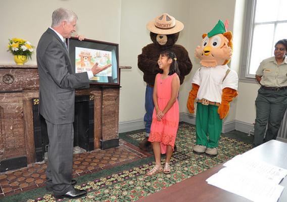 U.S. Forest Service Chief Tom Tidwell talks about a drawing by Joyce Qin, the 11-year-old Memphis-area girl who became the 2014 Smokey Bear & Woodsy Owl Poster Contest winner. Looking on from left to right is Smokey Bear, Woodsy Owl and Renee Green-Smith, National Information Center manager. (U.S. Forest Service/Dominic Cumberland)
