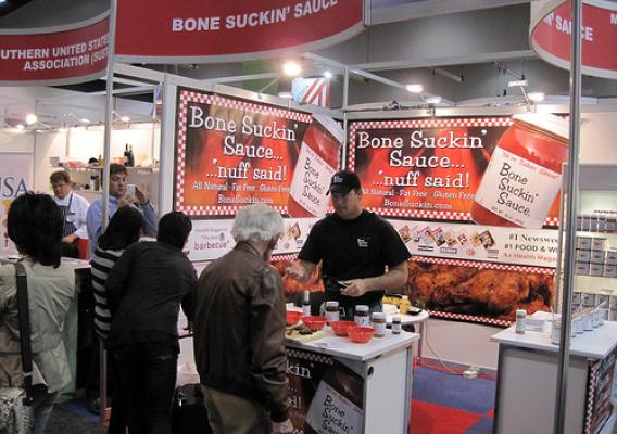 Pat Ford of Ford’s Gourmet Foods shares the company’s signature Bone Suckin’ Barbeque Sauce with visitors to a food show in Australia. Thanks in part to support from FAS market development programs, Ford’s now exports to more than 50 countries and 35 percent of their sales come from international markets.  (Photo courtesy of FAS)