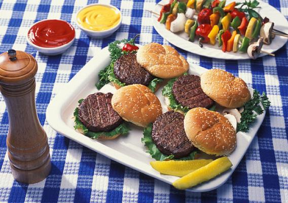 A plate of hamburgers beside vegetables on skewers, ketchup, mustard and a pepper shaker