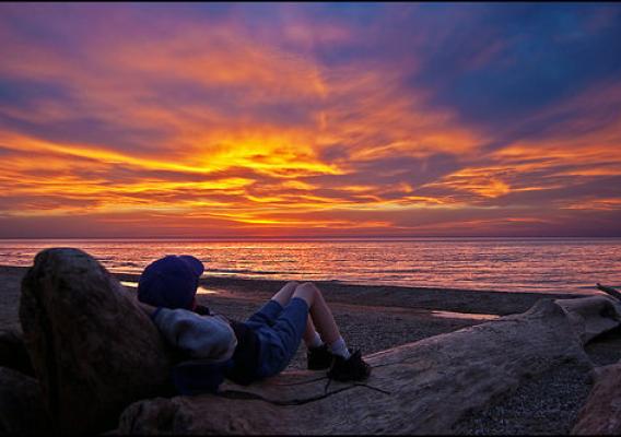 A youngster relaxes on a piece of driftwood, watching the beautiful sunset over Lake Michigan. Photo by Tom Gill.