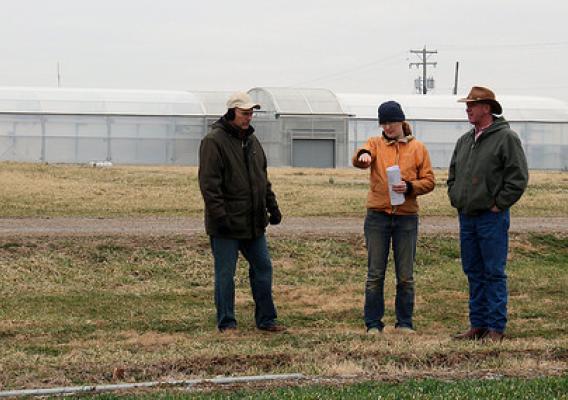 The University of Kentucky is using a Conservation Innovation Grant to improve the efficiency of seasonal high tunnels. NRCS and UK staff  view a water line with a high tunnel in the background. NRCS photo.