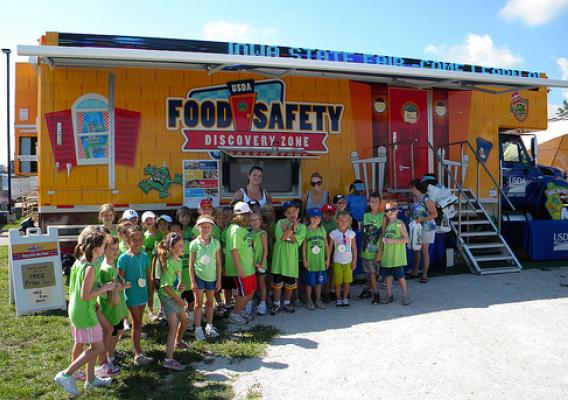 A school group poses in front of the Food Safety Discovery Zone after learning to Clean, Separate, Cook, and Chill.