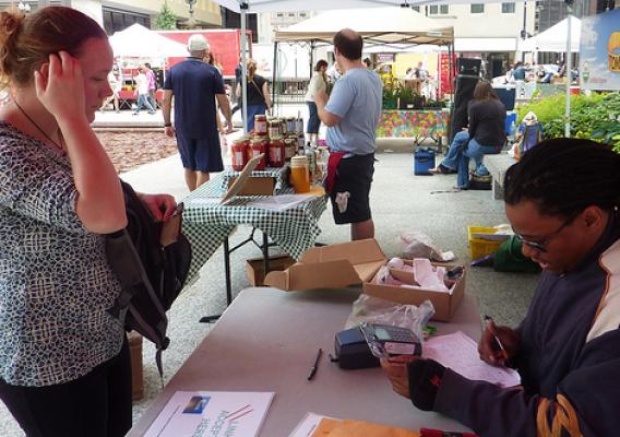 Corey Chapman, EBT Coordinator for City of Chicago farmers markets, processes a woman’s benefits card so she can purchase items at the market.