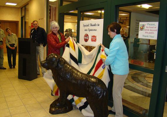 The life-sized statue of Seaman, the famed Newfoundland dog who accompanied the Lewis & Clark expedition, is unveiled at the Lewis & Clark Interpretive Center by (left) Margaret Halko, the widow of the statue's sculptor Joe Halko; and Carol Mungus, whose dog 'Windsor' stood as the model for Halko's creation. (USDA Forest Service photo) 