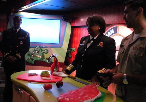 After having discussed the Separate station and importance not cross-contaminating Dr. Regina Benjamin and LTJG Micheal Bowens stand by and watch the demonstration for the Cook station being performed by LCDR Karen Munoz