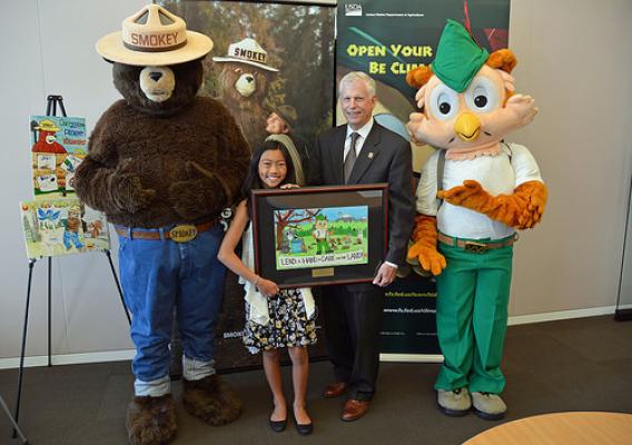 Audrey Morga, national winner of the 2015 National Smokey Bear and Woodsy Owl poster, standing with U.S. Forest Service Chief Tom Tidwell, Smokey Bear and Woodsy Owl