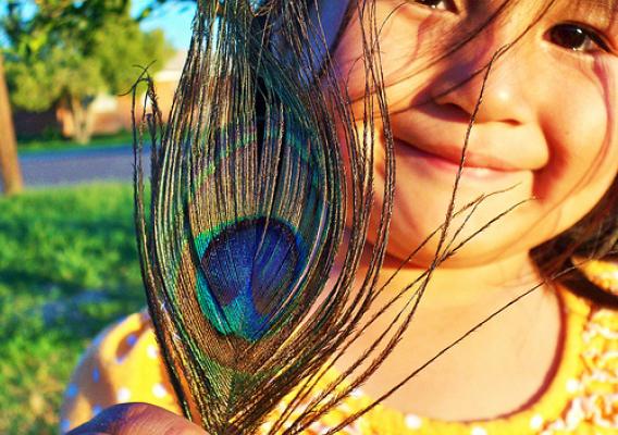 A young Tohono O’odham girl smiles and shows off a peacock feather.  The Tohono O’odham Community Action is working to create a healthy, sustainable and culturally-vital community for the Tohono O’odham Nation’s 28,000 members.  Photo by Cheryl Maze Walker.