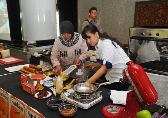Chef Ucu Sawitri invited one of the participants to work with her to prepare an "Apple Banana Roll" recipe using dehydrated potato flake, Washington apples, California raisins, and Washington apple juice.