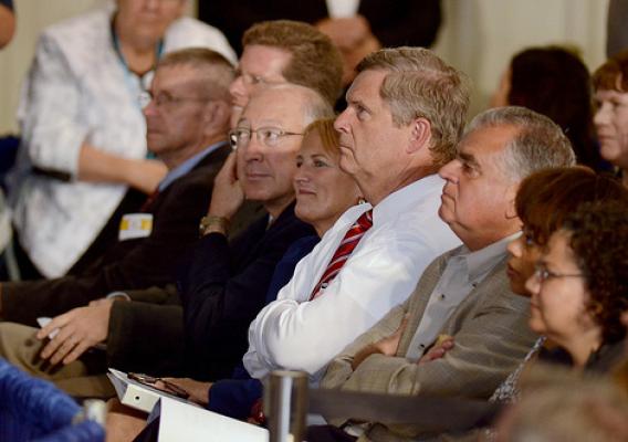Agriculture Secretary Tom Vilsack (center white shirt) listens to President Barack Obama speaking at the Northeast Iowa Community College for a White House Rural Economic Forum on August 16, 2011. Agriculture Secretary and chair of the White House Rural Council, Tom Vilsack, notes that the President’s visit will focus on agriculture’s contribution to the national economy, and how to create more jobs in rural America. USDA Photo by Lance Cheung. 