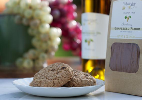 WholeVine gluten-free Chardonnay grape seed flour bag beside a plate of cookies and a bottle of wine with red and white grapes behind them
