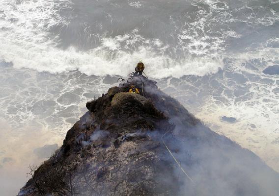Los Padres firefighter Kevin Poyner (facing camera) and John Knight of the Big Sur Volunteer Fire Brigade appear to have one foot “in the black” and the other in the Pacific Ocean. In reality, the two men have ample room between their position and the cliffs leading down to the beach.