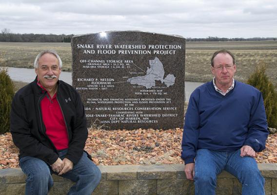 Doug Sorenson, Middle-Snake-Tamarac Rivers Watershed District board member, and Nick Drees, the district’s Administrator, sitting by the Richard P. Nelson Floodway monument. (NRCS photo/ Julie MacSwain)