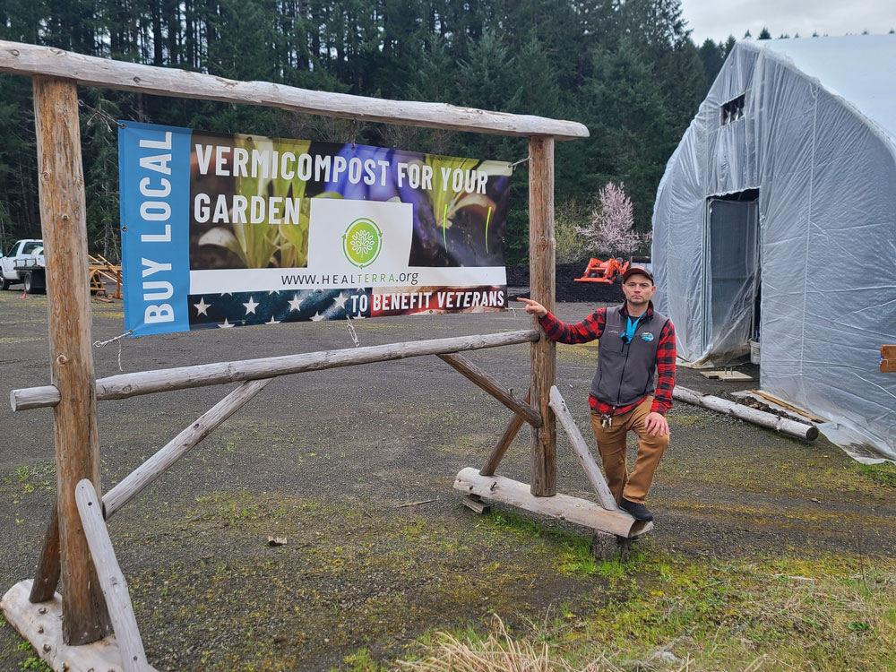A man pointing to a Vermicompost for Your Garden sign on a wooden stand